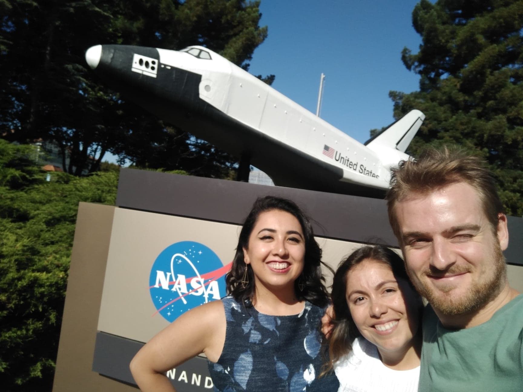 Sam Naef with two colleagues in front of a NASA sign and a space shuttle model