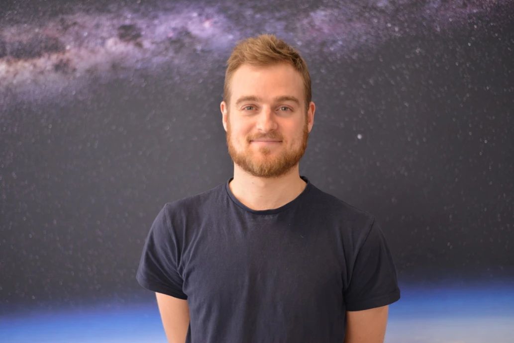 Sam Naef, physics tutor, smiling in front of a starry backdrop